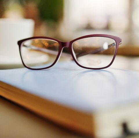 Rote Brille auf einem Buch, dahinter eine Kaffeetasse