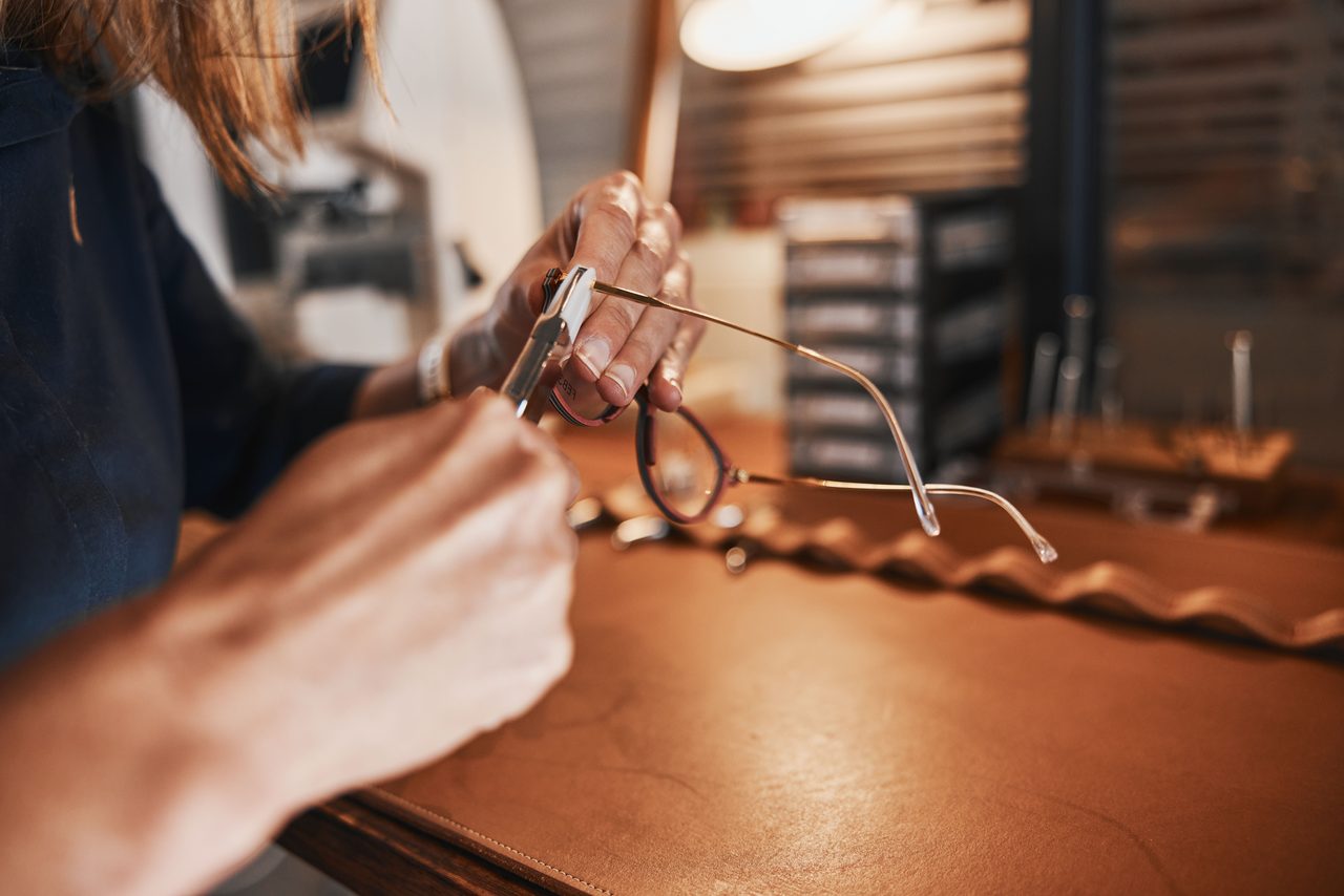 Hände richten mit einer Zange eine Brille auf einer Werkbank